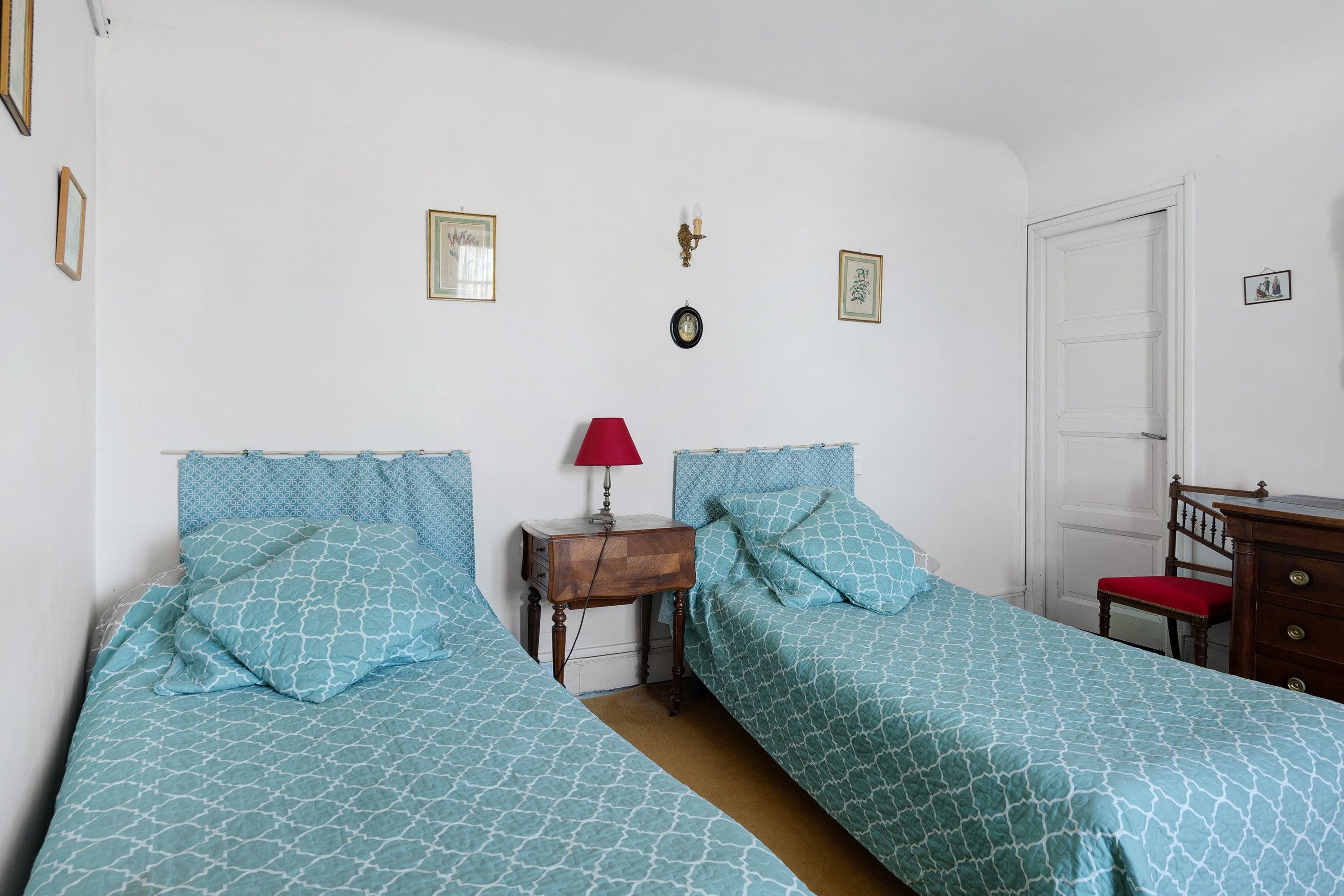 Een slaapkamer met twee bedden, een nachtkastje, een rode lamp en een houten dressoir.