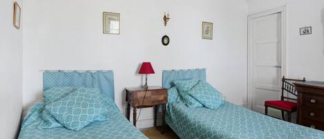 A bedroom with two beds, a nightstand, a red lamp, and a wooden dresser.