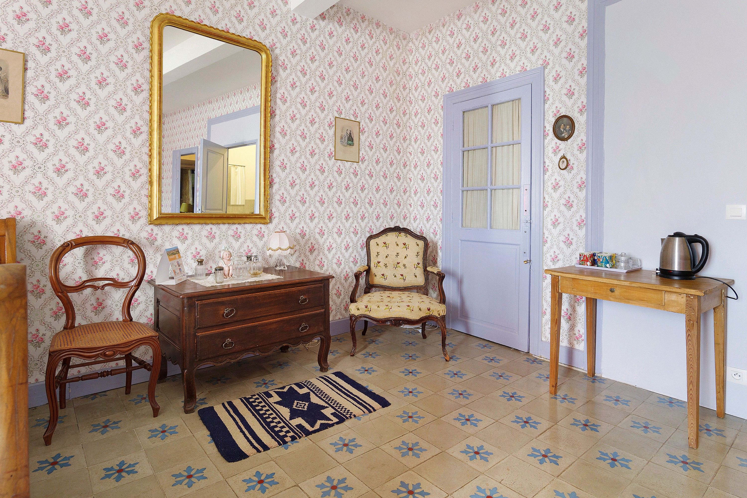 Una habitación con un aparador de madera, una silla, una mesa con hervidor y un espejo en la pared.