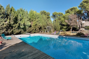 Une piscine dotée d’une terrasse en bois, entourée d’arbres et aménagée avec des chaises longues.