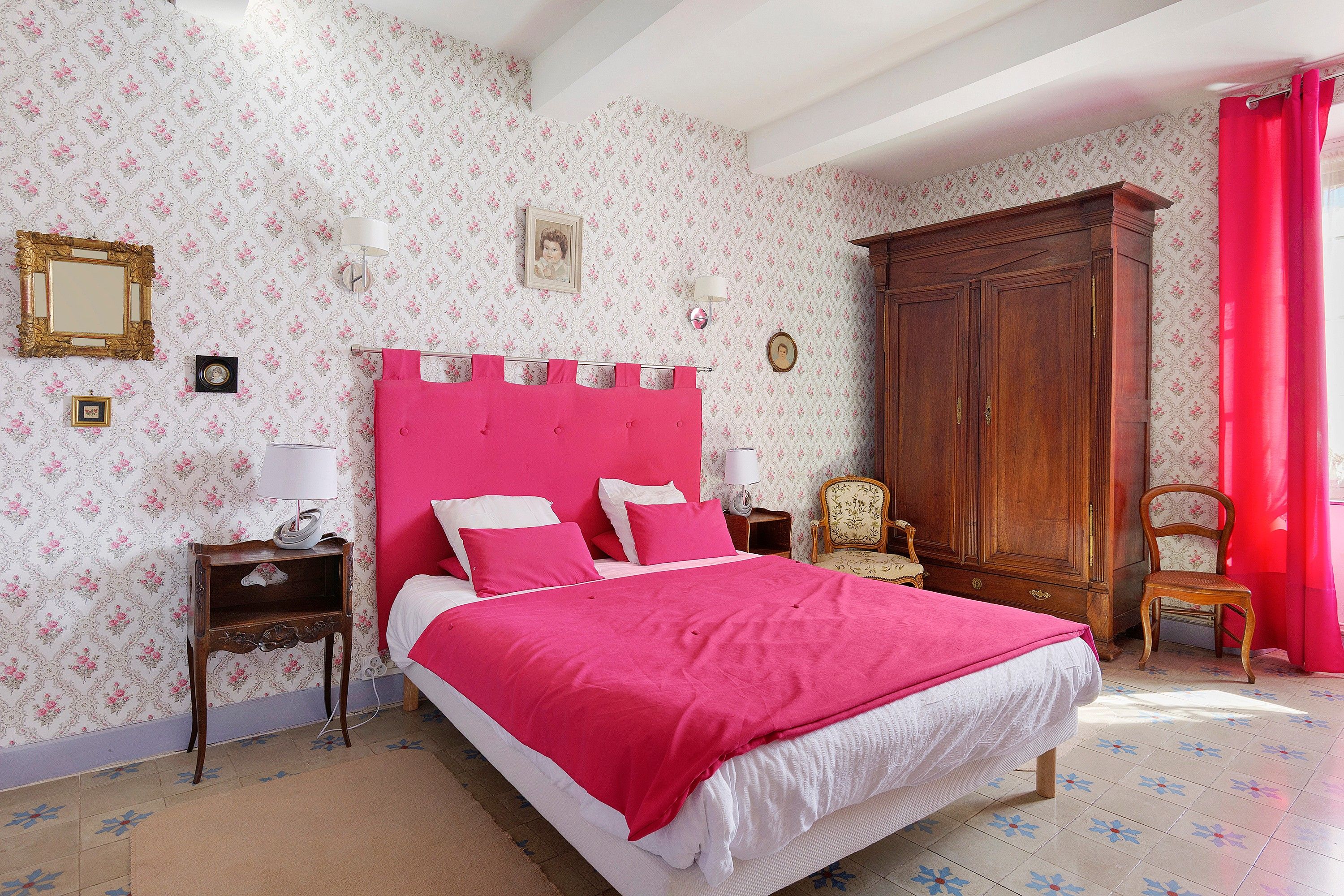 A bedroom with a large bed, a wooden wardrobe, and floral wallpaper.