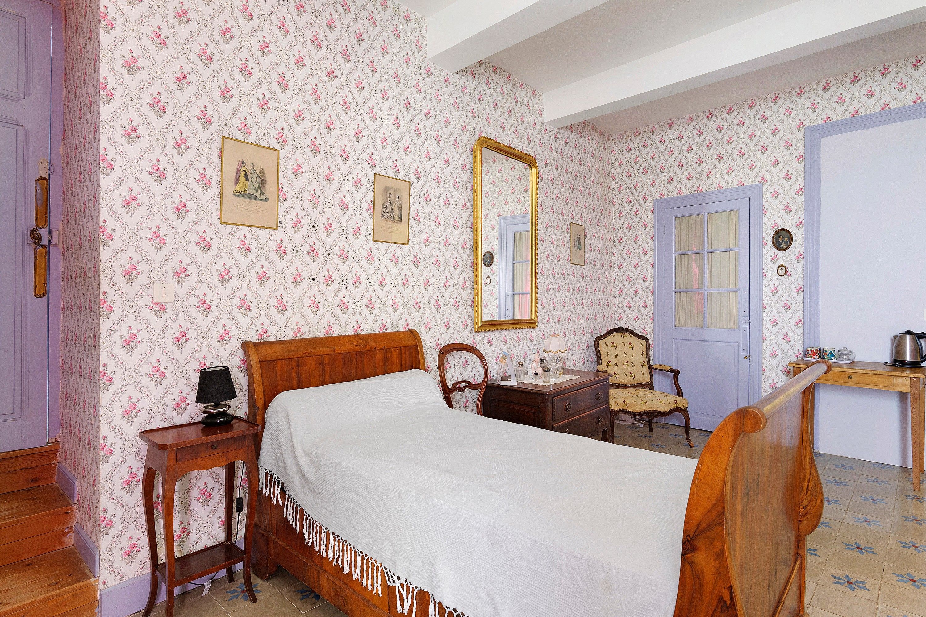 Ein Schlafzimmer mit einem hölzernen Bett, einem Nachttisch, einer Kommode, einem Stuhl, einem Schreibtisch und einer Tür.