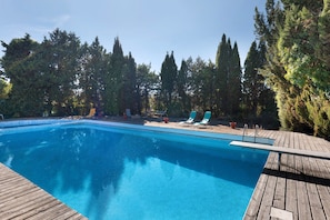 A swimming pool with a wooden deck, surrounded by tall trees.