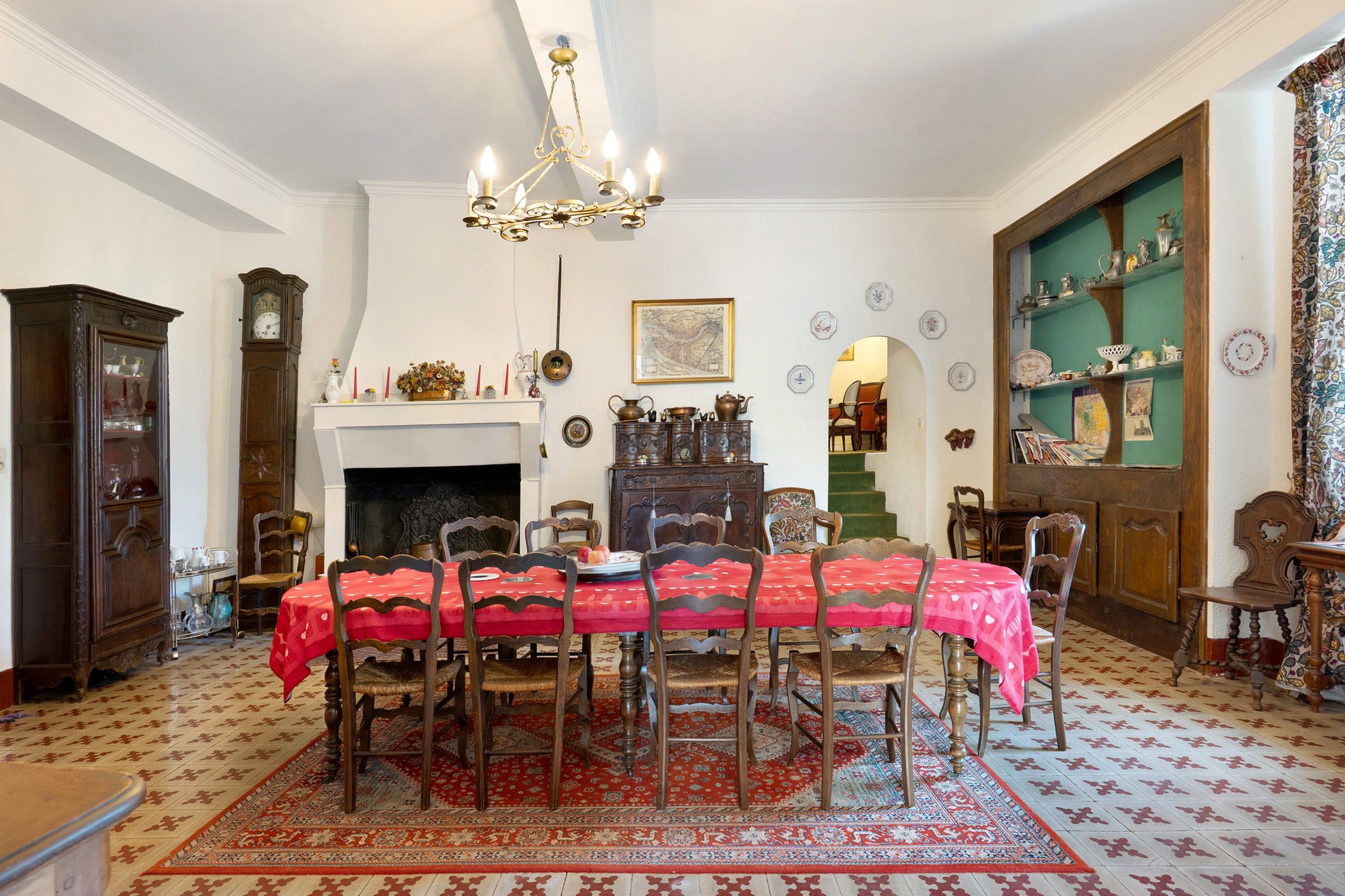 Ein traditioneller Essraum mit einem runden Tisch, Stühlen, einer Chandelüster, einem Kamin und einer grünen Wand mit Regalen.