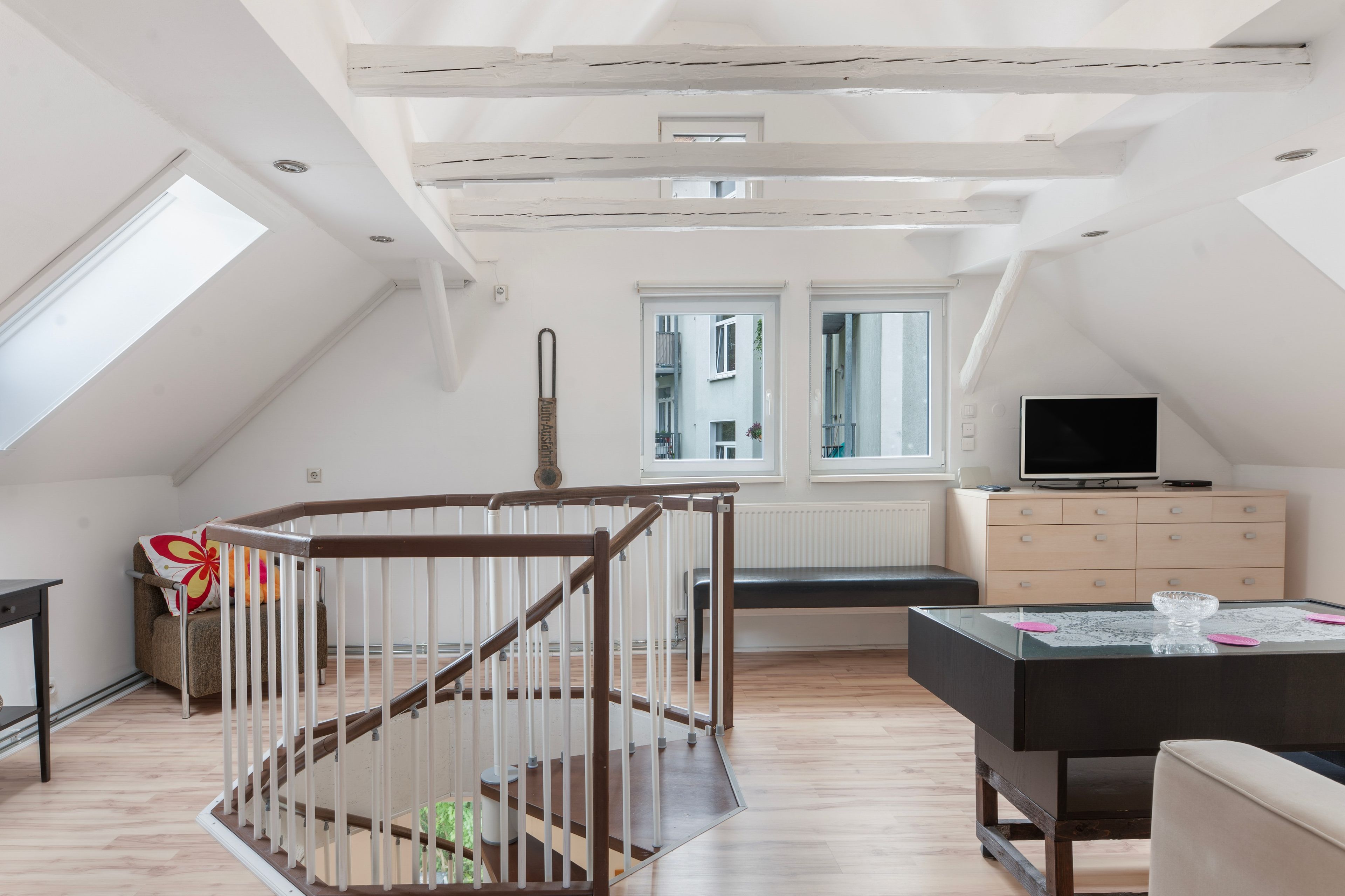 A modern loft apartment with a wooden staircase, a flat-screen TV, and a dining area.