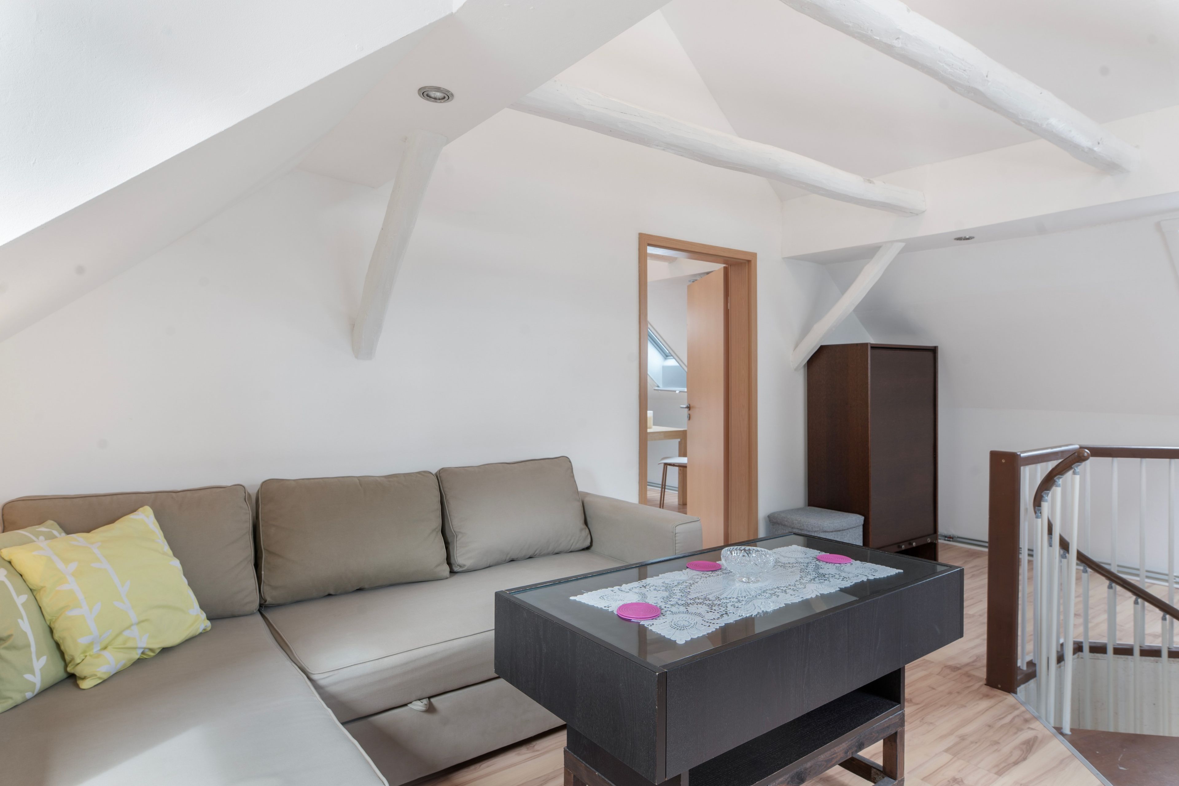 Ett modernt sovrum i loftstil med ett sluttande tak, en soffa med kuddar, ett soffbord i glas och en garderob i trä.