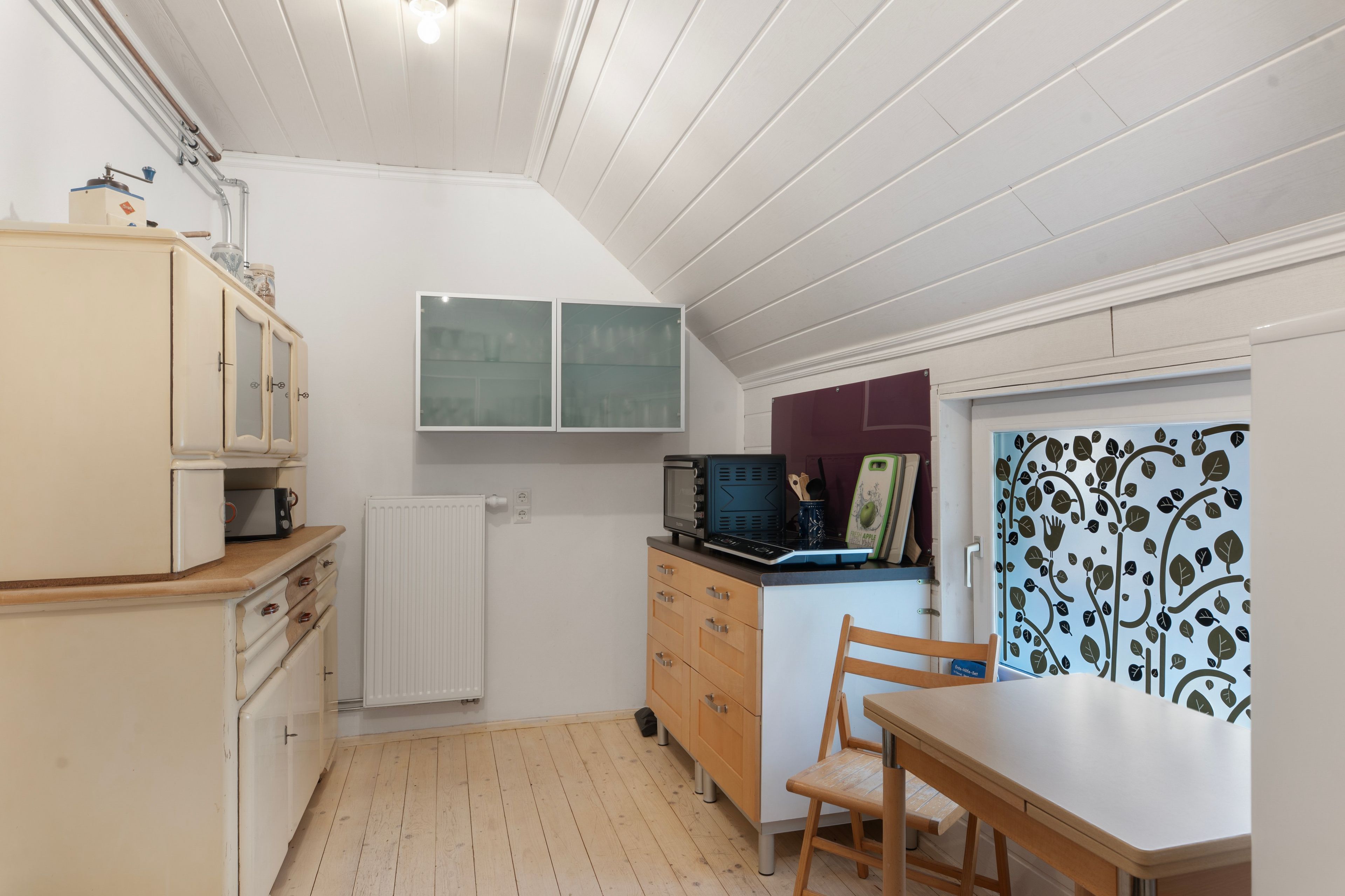 Eine kompakte Küche mit Holzausbau, einem eingebauten Backofen und einer kleinen Essecke mit Holztisch und Stuhl.