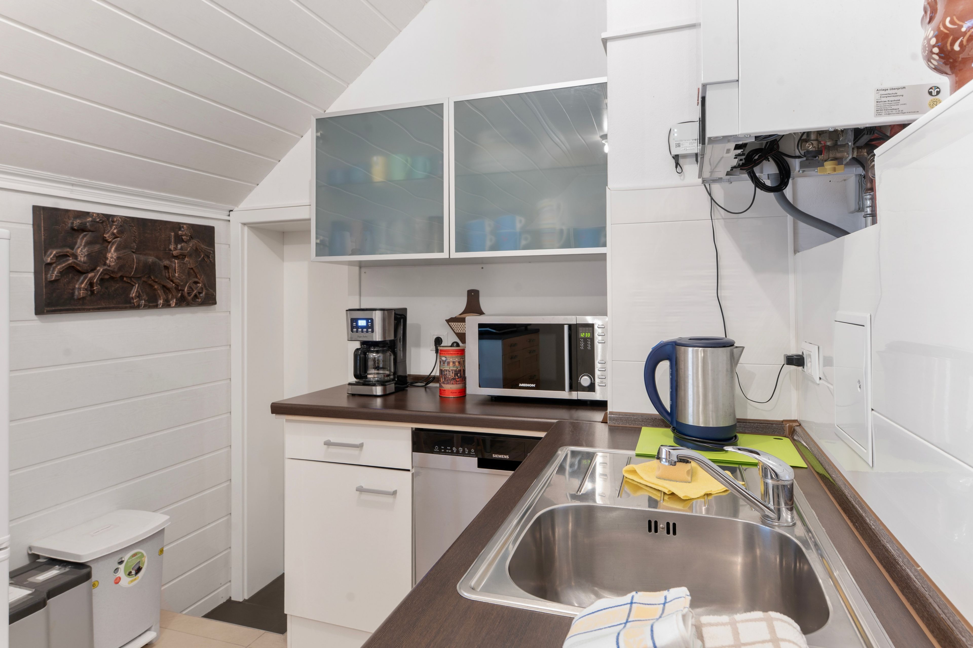 Cocina compacta con lavavajillas, cafetera, microondas, hervidor y un lavabo con pileta de acero inoxidable.