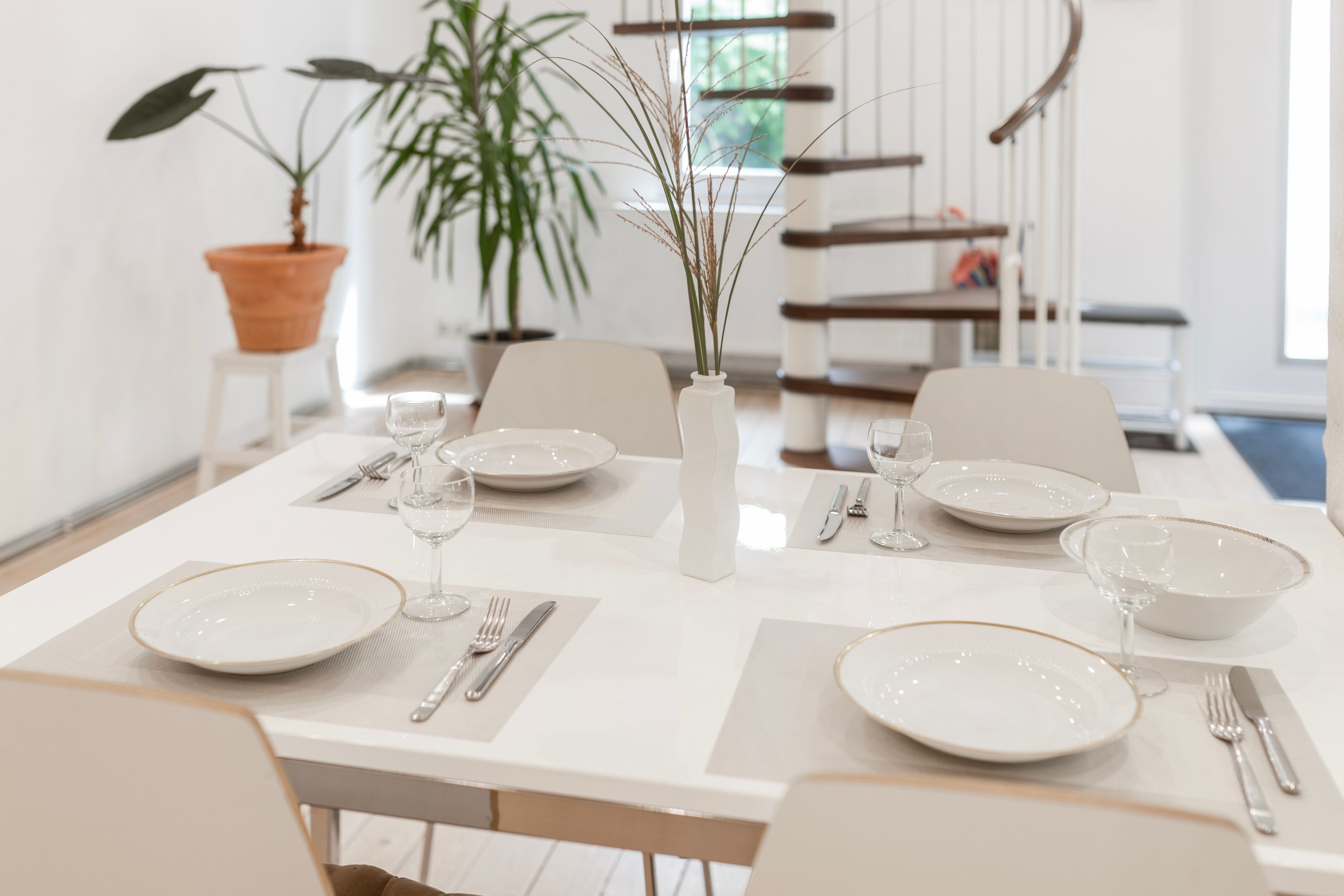 A dining table set with plates, cutlery, and glasses, surrounded by chairs.