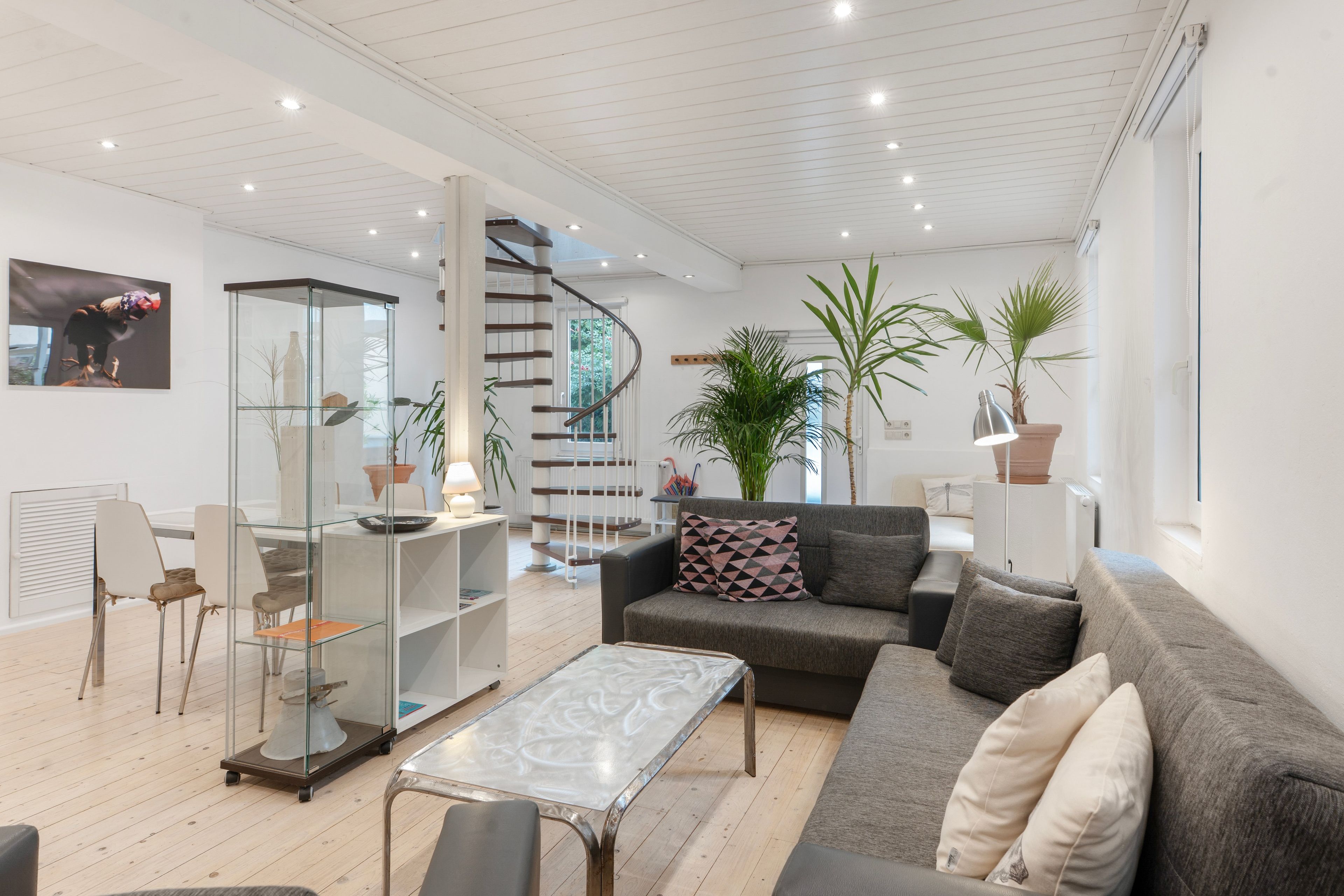 Una sala de estar moderna con un vitrina de vidrio, un sofá gris, una mesa de centro y una escalera.
