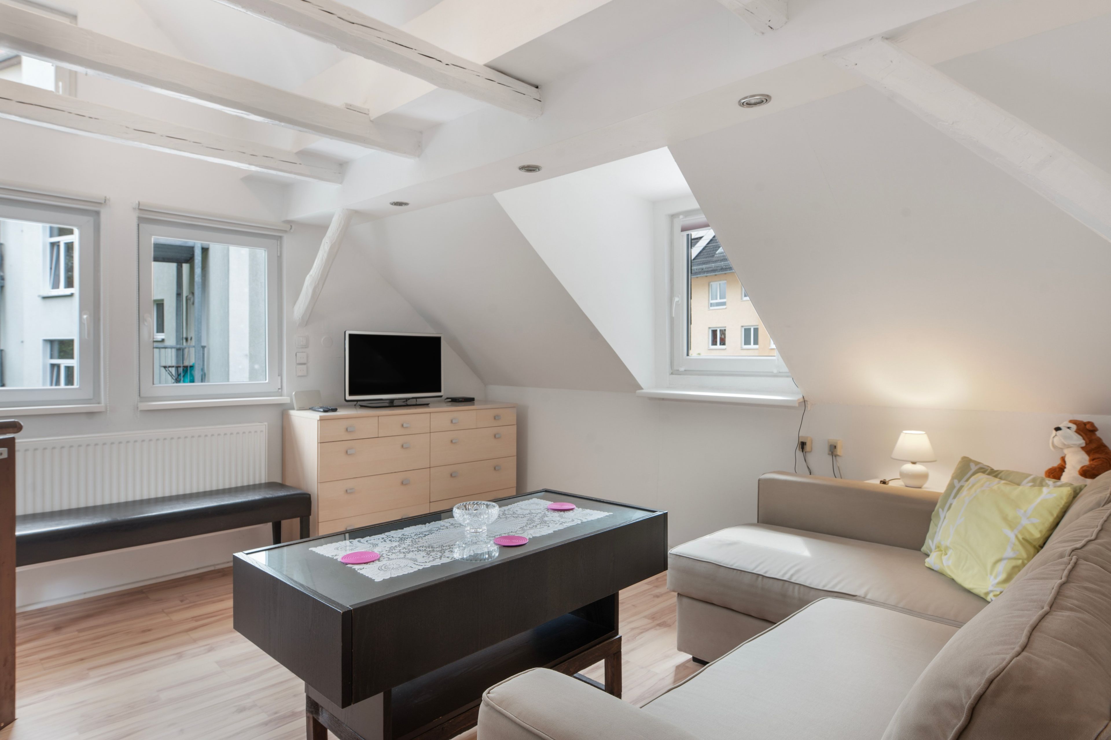 Ein modernes Wohnzimmer mit Dachstockdecke, Flachbildfernseher, Glastisch, Sofa und einer Lampe.