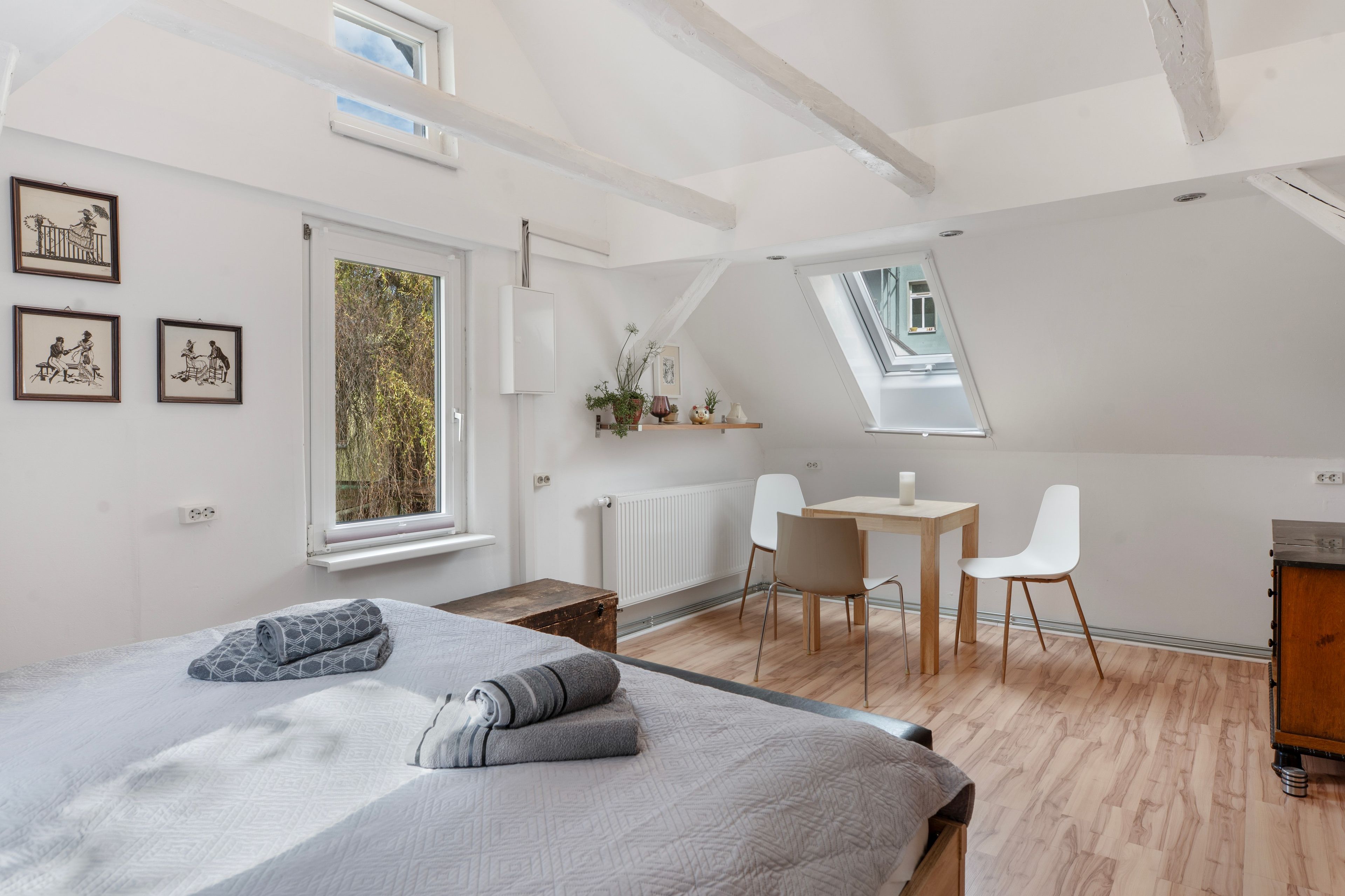 Ett modernt sovrum med ett tak i loftstil, en säng med hoprullade handdukar, ett skrivbord med en stol och konstverk på väggarna.