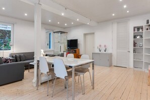 A modern living room with a dining area, a flat-screen TV, and a bookshelf.