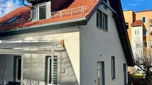 Una casa de un piso con techo a dos aguas de tejas rojas, un balcón pequeño y un camino de entrada pavimentado.