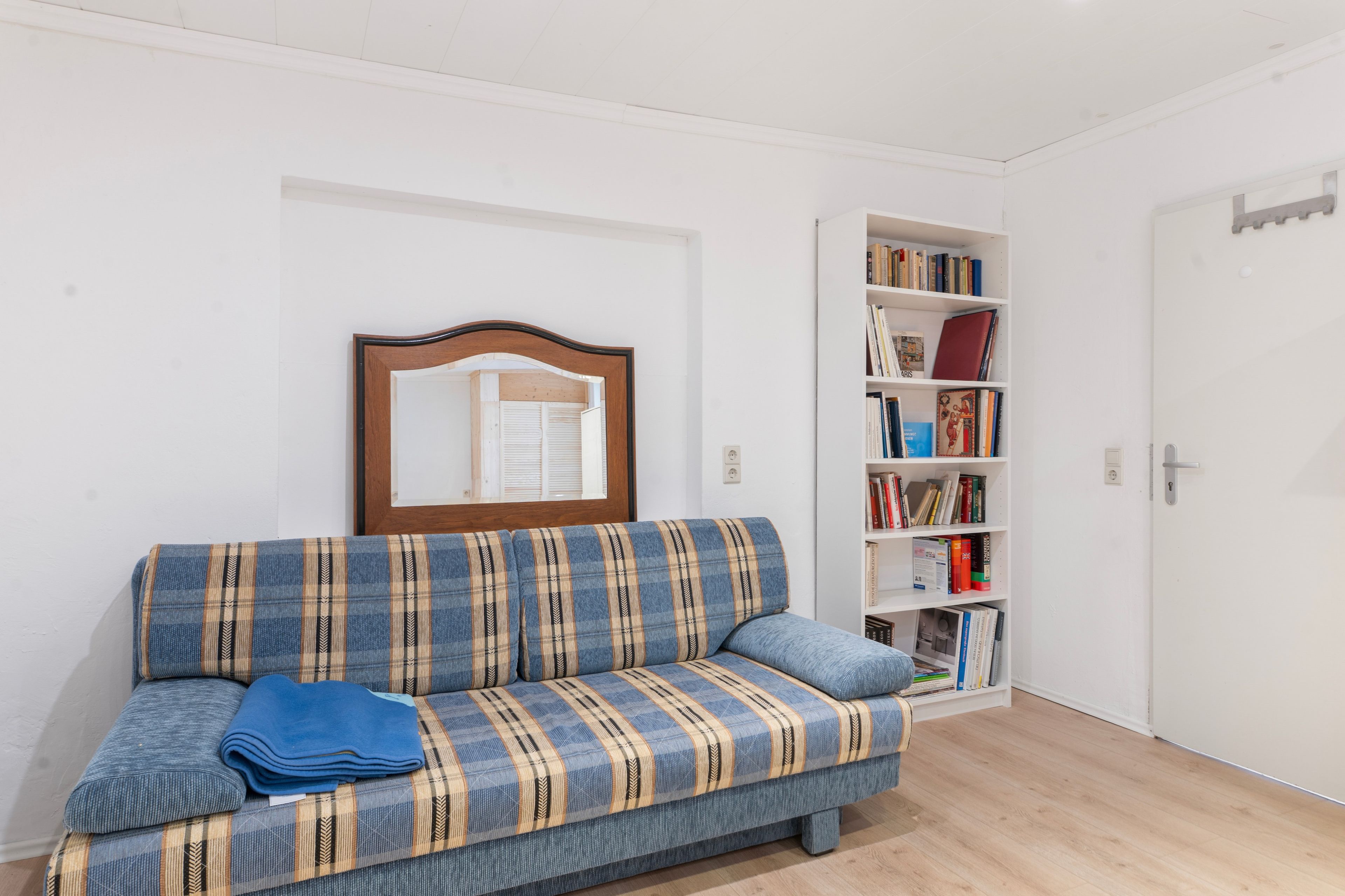 Ein Zimmer mit einer Couch, einem Bücherregal und einer Tür.