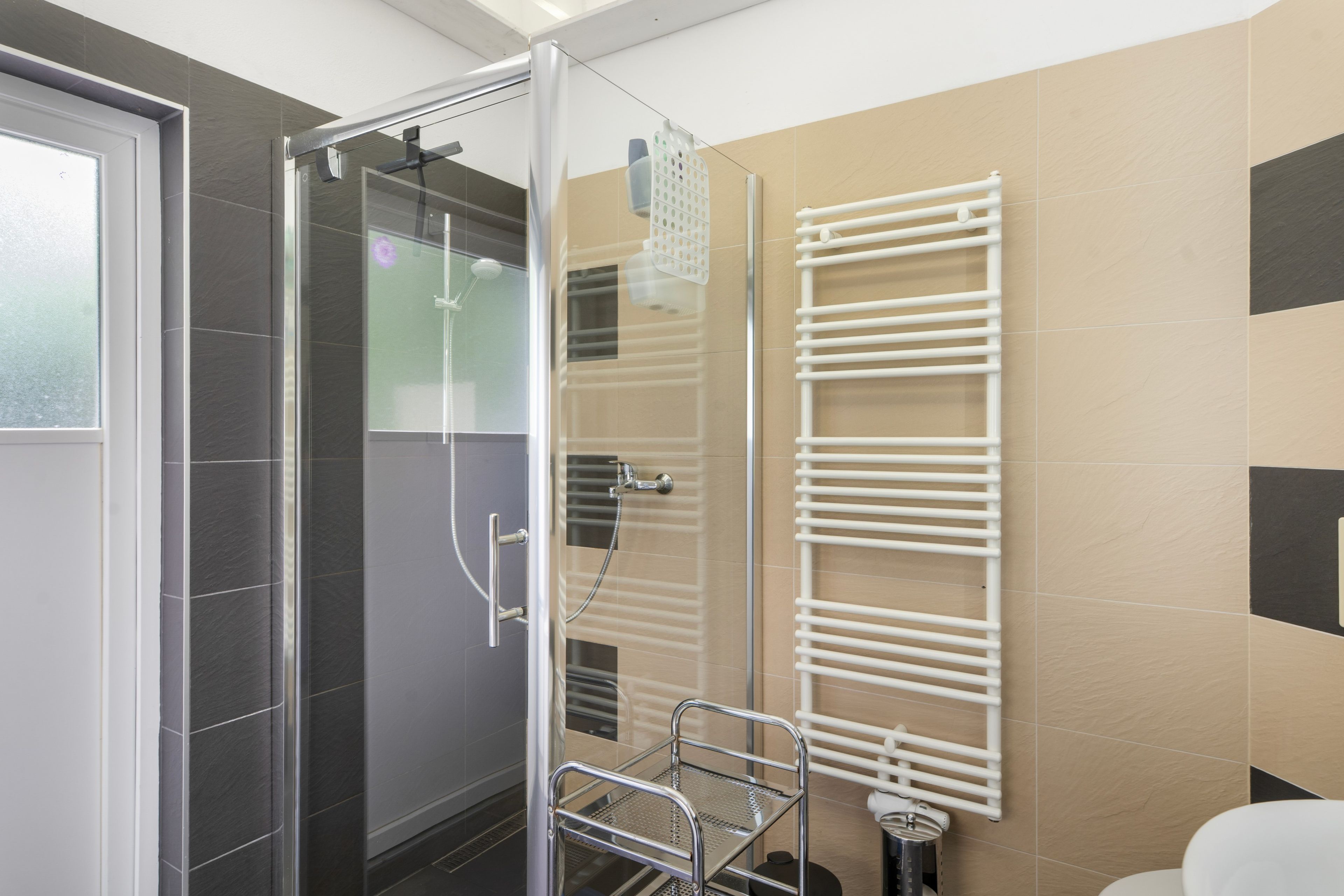 A modern bathroom with a glass shower enclosure, a white towel rack, and a toilet.