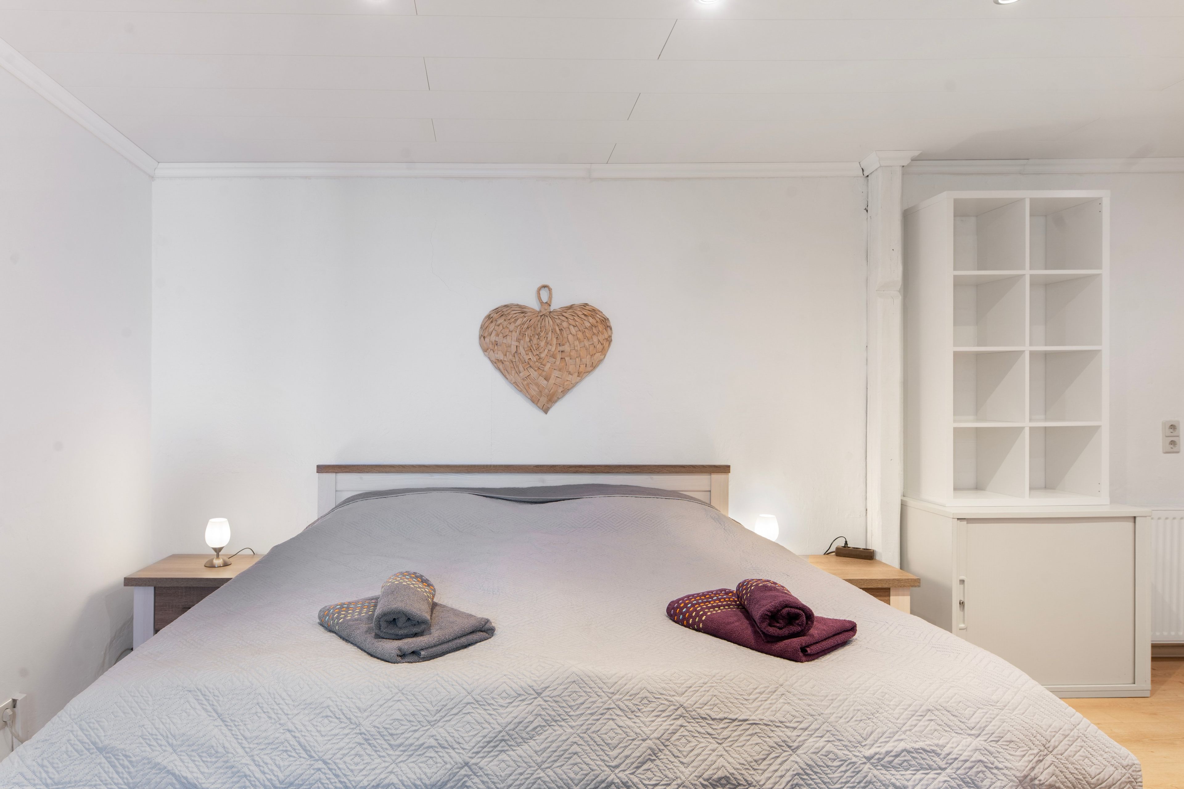 Een slaapkamer met een bed, nachtkastje, wanddecoratie in de vorm van een hart en een inbouwkast.