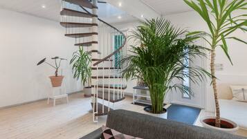 Ein modernes Interieur mit einer Wendeltreppe, einem grauen Sofa und verschiedenen Blumentöpfen.