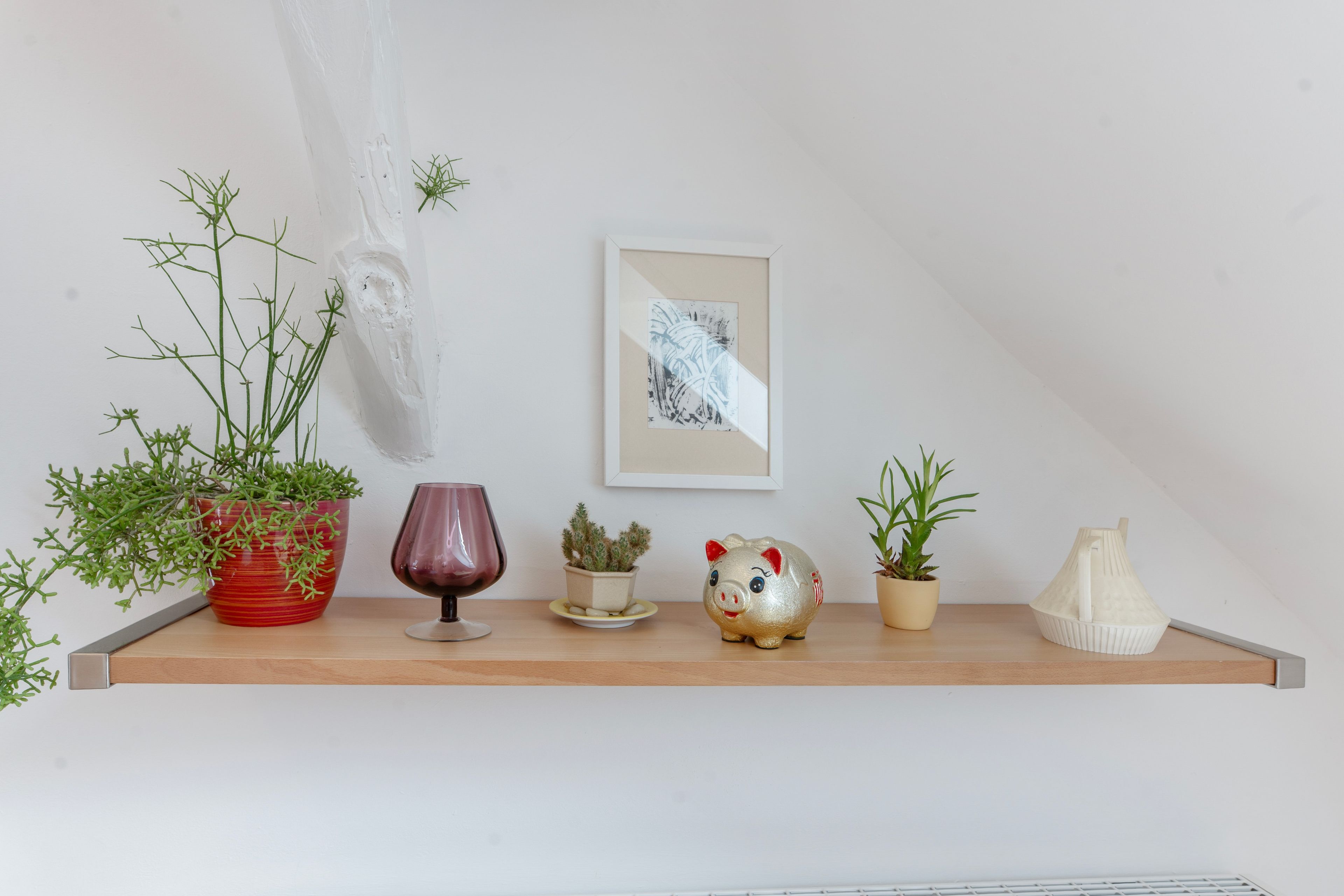 A shelf with various decorative items including plants, a piggy bank, and a framed artwork.