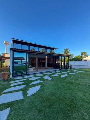 Een modern huis met een glazen gevel, een terras en uitzicht op de oceaan.