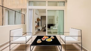 Un appartement moderne doté d’un coin repas avec une table noire et des chaises blanches, d’un balcon avec une rambarde en métal et d’une vue sur l’intérieur, visible à travers une porte en verre.