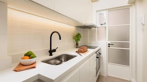 Une cuisine moderne avec des meubles blancs, un évier en acier inoxydable et un four encastré.