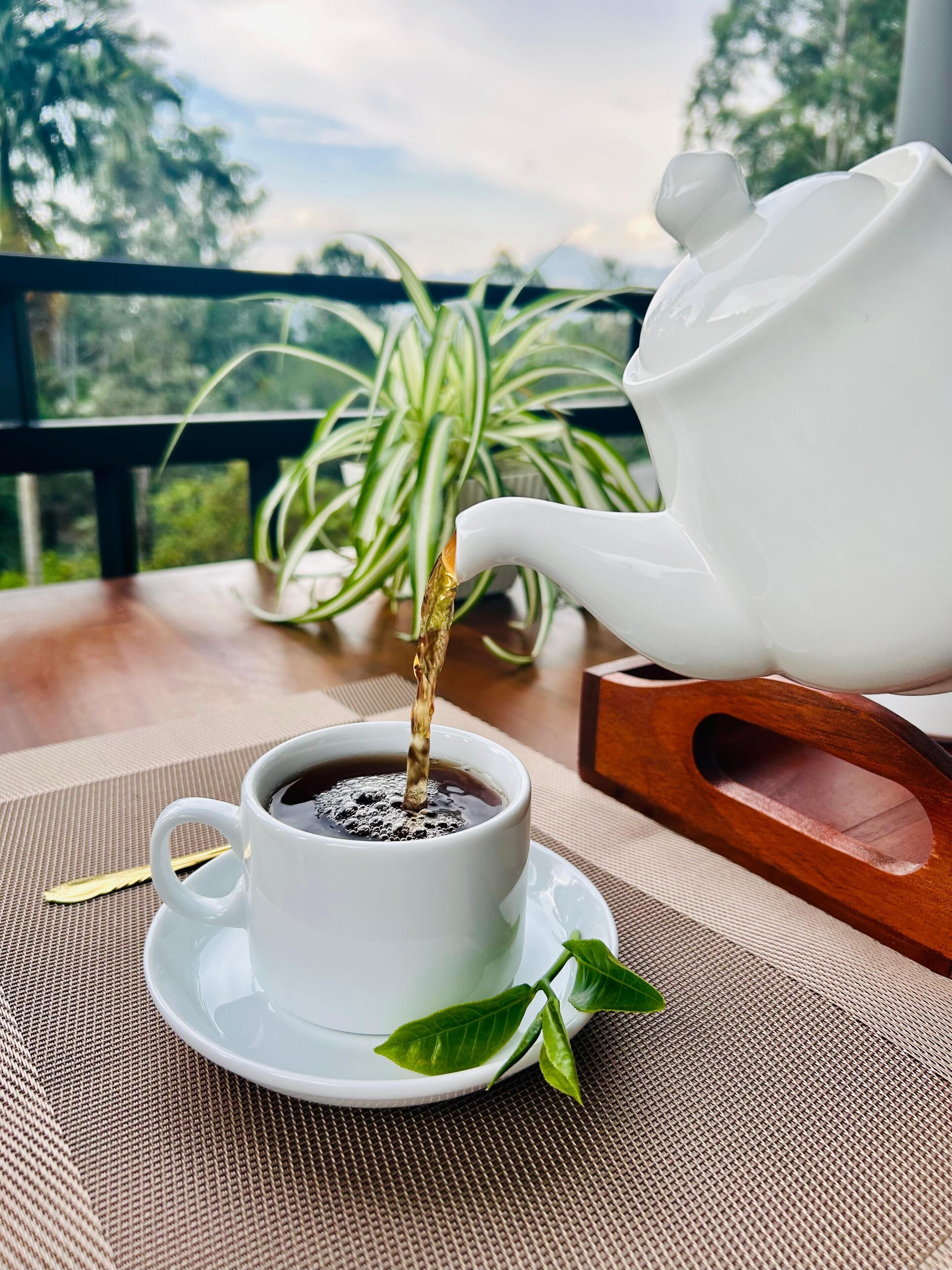 A white teapot pouring tea into a white cup on a table with a woven placemat.