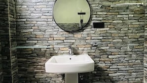A bathroom with a stone wall, a round mirror, and a pedestal sink. - Leafveil Ella (Ella)