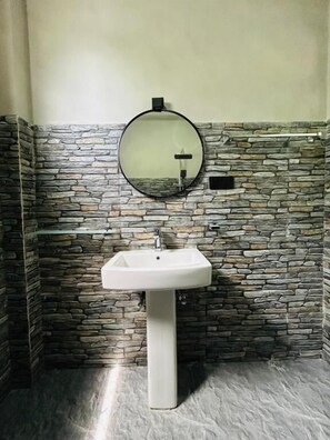 Un baño con pared de piedra, un espejo redondo y un lavamanos sobre pedestal.