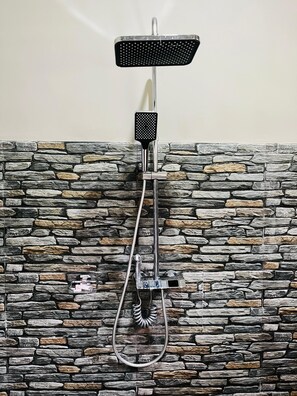Un cabezal de ducha con un accesorio de mano, fijado a una pared con diseño de piedra.