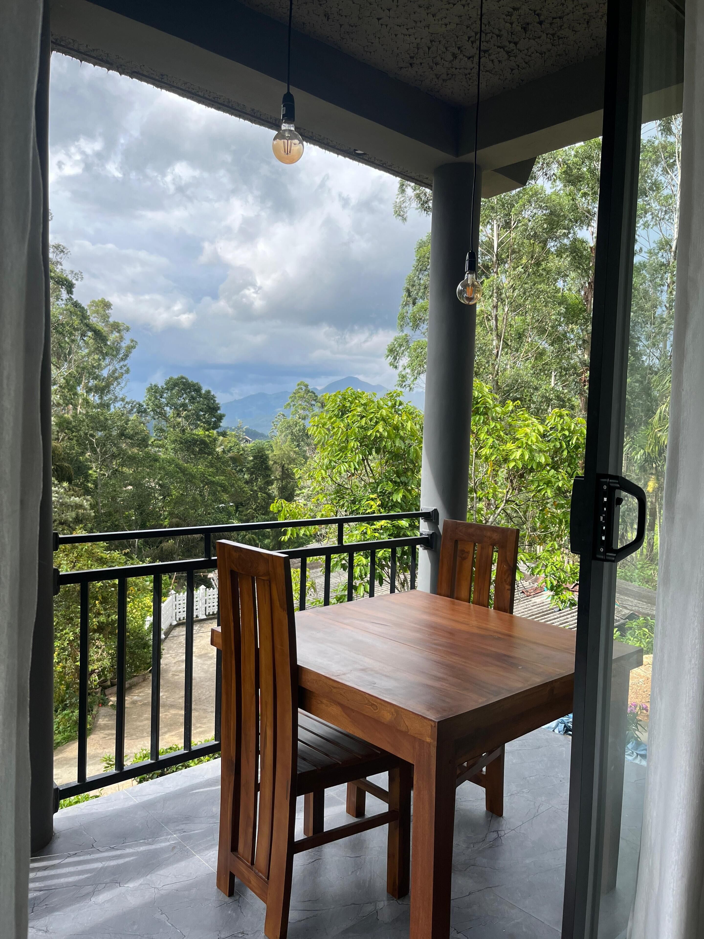 Una mesa y sillas de madera en un balcón con vistas a árboles y montañas.