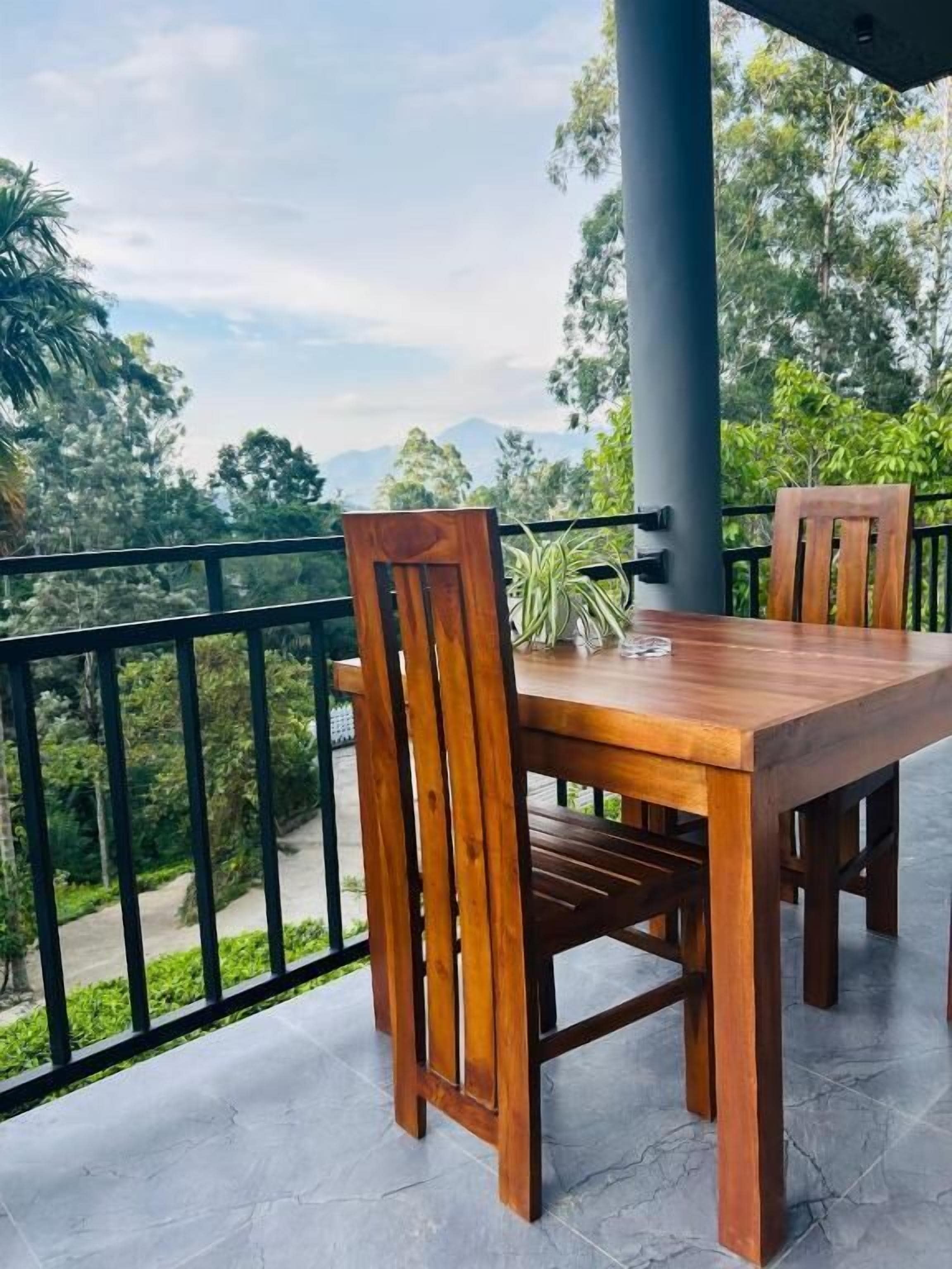 A wooden table and chairs on a balcony with a view of trees and mountains.