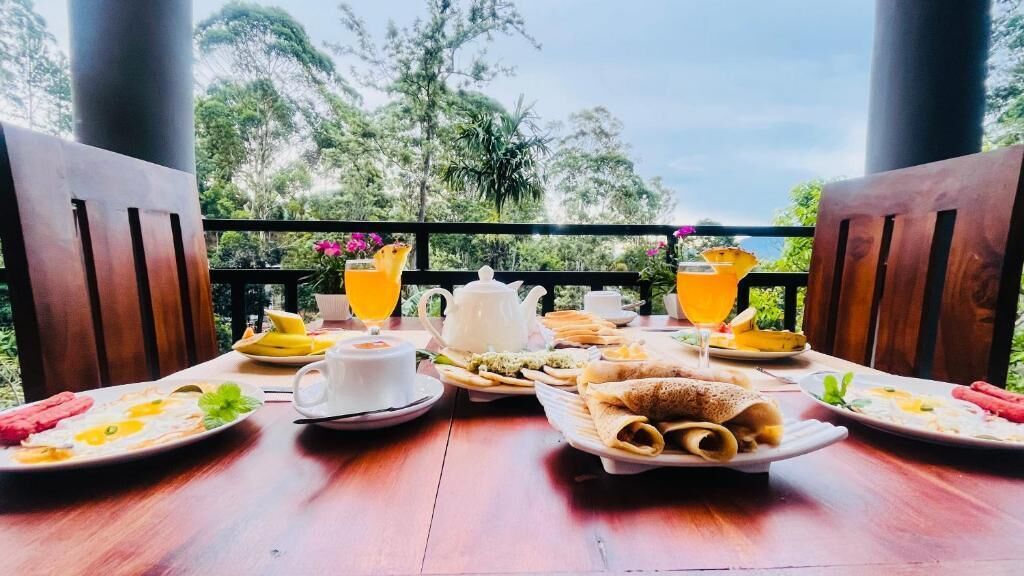 A breakfast table set outdoors with plates of food, cups, and a teapot.