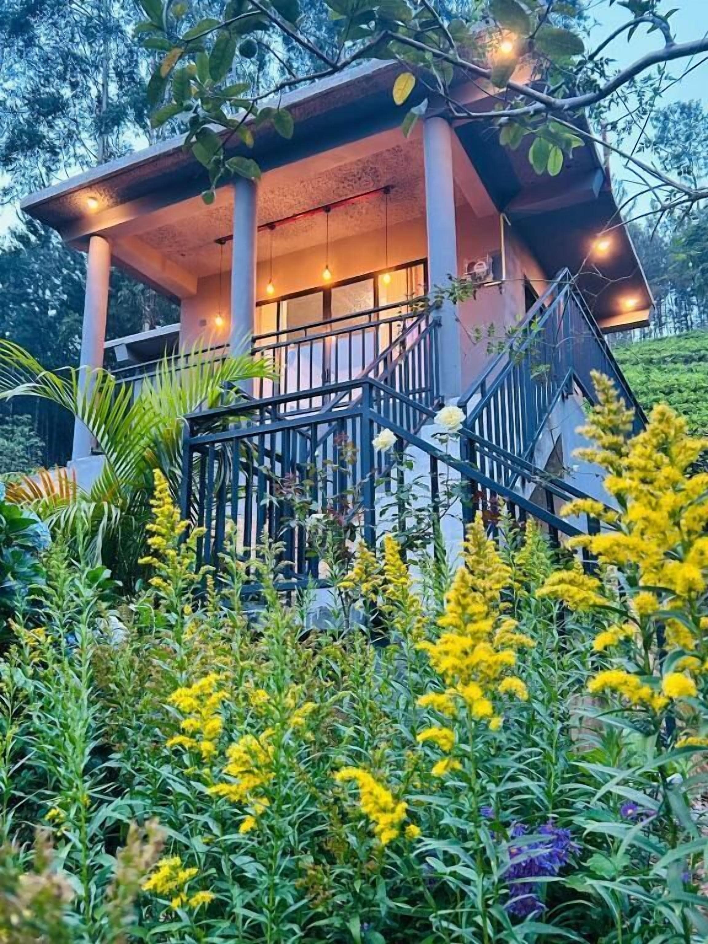 A two-story building with a balcony, surrounded by a garden with yellow flowers.