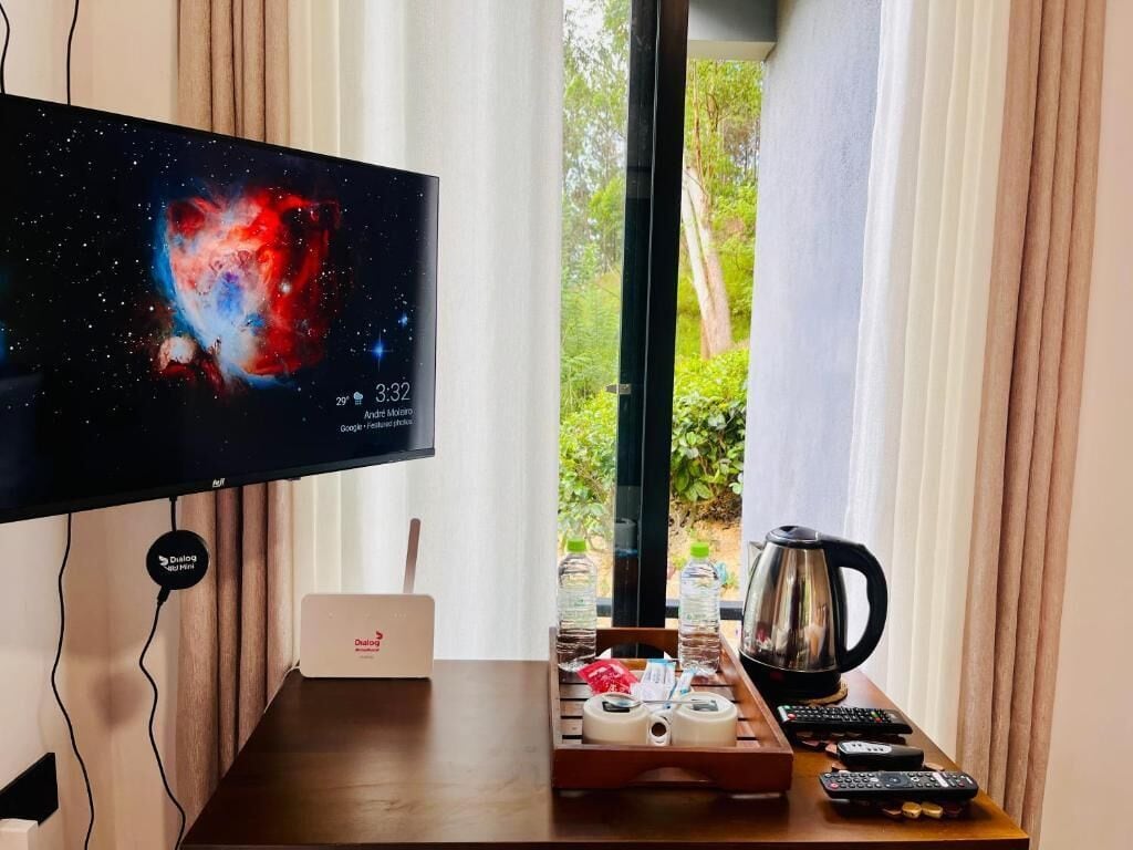 Een kamer met een televisie waarop een nevel afgebeeld is, een koffiezetapparaat, afstandsbedieningen en een dienblad met toiletartikelen.
