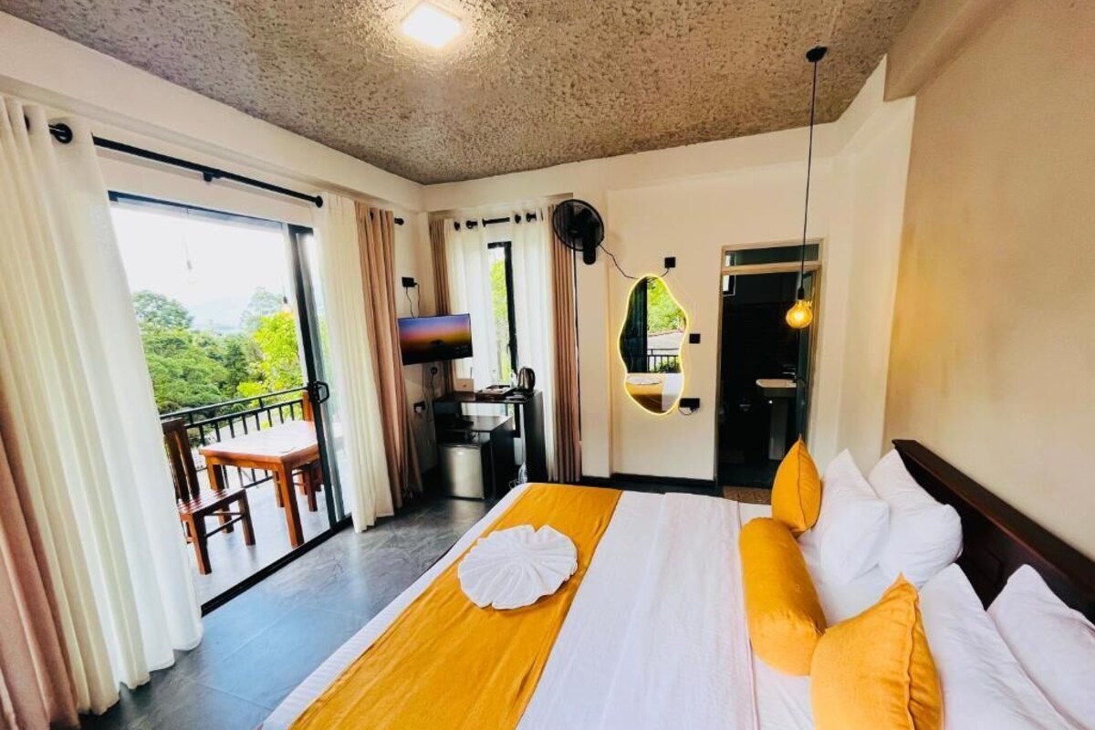 Habitación de hotel con una cama grande, un balcón, kitchenette y vistas al verdor.