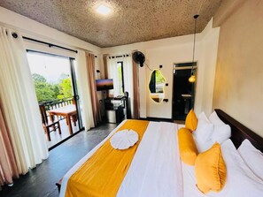 Habitación de hotel con una cama grande, un balcón, kitchenette y vistas al verdor.