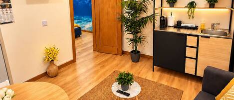 A compact living space with a dining area, a sofa, a kitchen area with a sink, and a TV mounted on the wall.