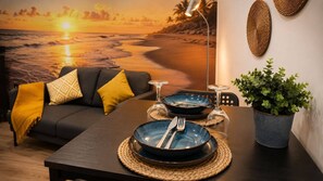 A dining area with a table set for two, a sofa with cushions, a potted plant, and a wall mural of a beach scene. - 77 Lisbon Design Studio near Airport (Sintra)