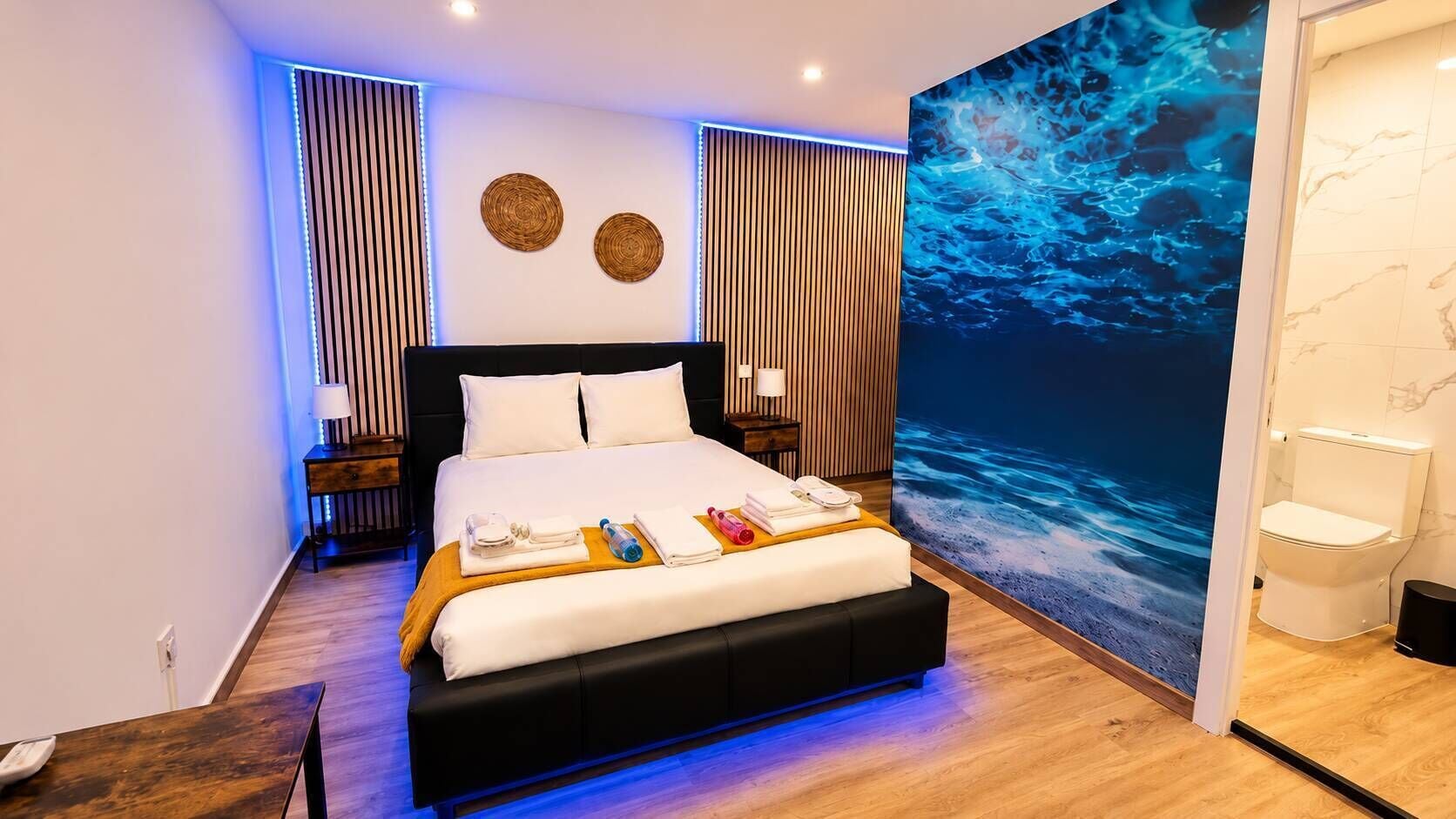 Una habitación de hotel moderna con una cama grande, una mesita de noche, un televisor montado en la pared y un baño visible a través de una puerta abierta.