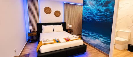 Una habitación de hotel moderna con una cama grande, una mesita de noche, un televisor montado en la pared y un baño visible a través de una puerta abierta.