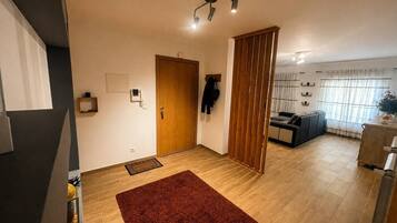 A modern living room with a wooden door, a red rug, a sofa, and a kitchen area with a refrigerator.
