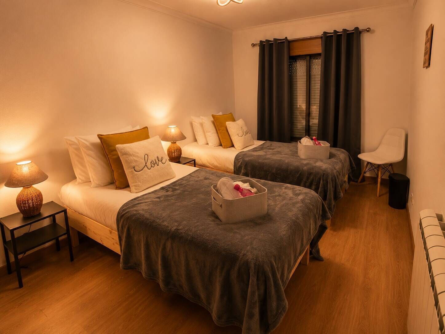 Una habitación de hotel con dos camas, una mesita de noche con lámpara, una silla y un ventanal con cortinas.