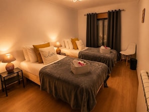 Una camera d'albergo con due letti, un comodino con una lampada, una sedia e una finestra con tende.