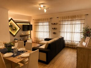 Un soggiorno moderno con un divano, un tavolo da pranzo per quattro persone, una TV a schermo piatto montata a parete e una lampada a sospensione.