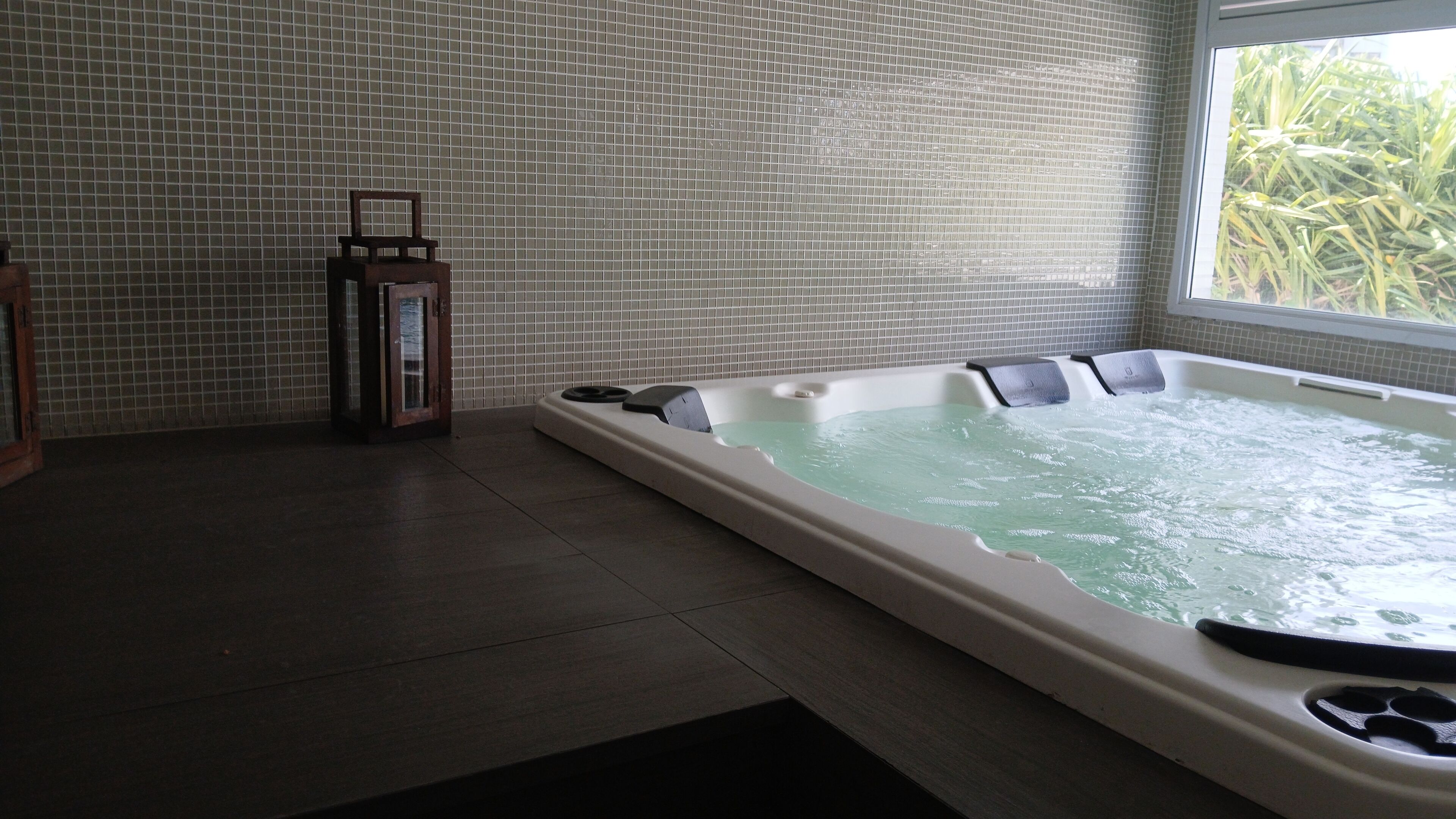 A spa room with a hot tub, tiled walls, and a window with a view of greenery.
