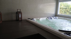 Sala de spa com banheira de hidromassagem, paredes azulejadas e janela com vista para o verde.