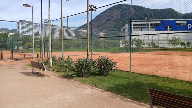 Cancha de tenis cercada con un banco y un camino que la conecta.