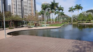 Un parque con un estanque, bancos, un área de juegos y edificios altos al fondo.