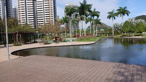 Um parque com lago, bancos, parque infantil e edifícios altos ao fundo.